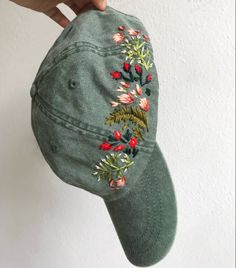 someone is holding up a green hat with embroidered flowers on the front and side of it