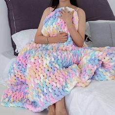 a woman sitting on top of a bed covered in a colorful knitted throw blanket