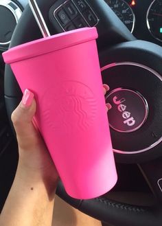 a person holding a pink starbucks cup in their hand next to a car steering wheel