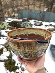 a person holding up a bowl in the snow with a pen sticking out of it