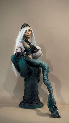 a doll with white hair sitting on top of a statue