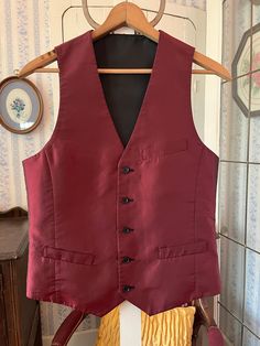 This handsome vest is burgundy with a black sheen/shift on one side and solid black on the other side! It has the original buttons, with three outer pockets on the burgundy side (two of them haven't been opened/unstitched yet) and one chest pocket on the black side. The measurements, taken with the vest lying flat, are: shoulder to shoulder, 12 inches; armpit to armpit, 19 inches; length, 25 1/2 inches in front and 22 inches in back; bottom edge, 17 1/2 inches. In very good condition. Burgundy Vest Outfit Men, Classic Red Vest For Fall, Classic Sleeveless Solid Outerwear, Classic Red Vest For Workwear, Classic Red Sleeveless Vest, Classic Red Sleeveless Outerwear, Formal Red Vest For Fall, Fitted Sleeveless Vest With Pockets, Red Fitted Sleeveless Outerwear