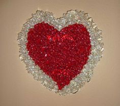 a red and white heart made out of glass beads on a beige wall with light brown background