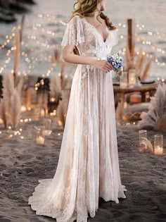 a woman in a wedding dress standing on the beach with candles and lights behind her