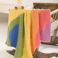 a crocheted blanket with a teddy bear sitting on top of it next to a rocking chair