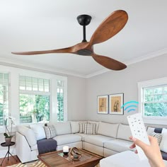 a person holding a remote control in front of a living room with a ceiling fan