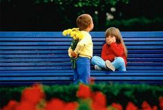 two children sitting on a park bench with flowers in their hands and looking at each other