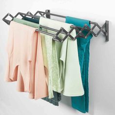 clothes hanging on a rack in front of a white wall with green and pink towels