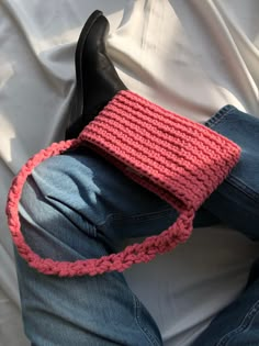 a person laying on top of a white sheet wearing jeans and a pink knitted purse