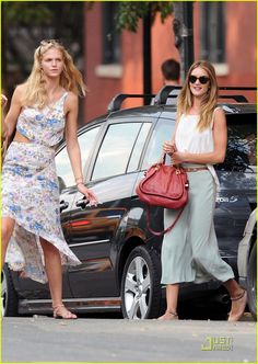 two women are walking down the street with one carrying a handbag and another holding a purse