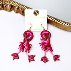 These earrings include multiple color pink beads and a gold detailing. Hanging from the bottom of the flamingo shaped beaded pendant has dangling legs. These earrings are pictured leaning agasint a gold mirror on a white background. Bohemian Dangle Beaded Earrings For Vacation, Beach Earrings With Dangling Beads, Bohemian Jewelry For Beach Season Parties, Summer Beach Beaded Earrings, Summer Vacation Drop Earrings, Summer Beach Beaded Earrings With Dangling Beads, Bohemian Beach Season Party Jewelry, Fun Beach Season Jewelry For Vacation, Trendy Earrings For The Beach Season