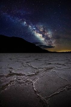 the night sky is filled with stars above a desert area, and there are mountains in the background