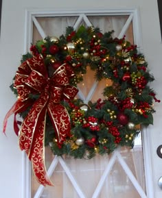 a christmas wreath hanging on the front door with red and gold ornaments around it,