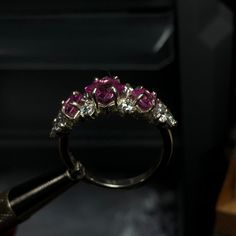 A beautiful cluster ring, set with three princess cut gemstones surrounded by ten round cut accents. This ornate ring is crafted with elegancy and designed to draw the eyes in. Pictured is three princess cut Pink Sapphires and accented with cubic zirconia. A plethora of stones are available for selection and the ring can be customized/mixed and matched with up to 13 different gemstones on one ring! Disclaimer: she tends to tarnish easy in between the gems, so a good chemical cleaner or toothbrus Cluster Ruby Rings With Diamond Accents, Ruby Cluster Rings With Diamond Accents, Elegant Three Stone Cluster Diamond Ring, Wedding Ruby Cluster Ring With Diamond Accents, Wedding Silver Ruby Ring With Accent Stones, 14k White Gold Cluster Jewelry With Prong Setting, Diamond Cluster Birthstone Ring With Accent Stones, Marquise Cut Ruby Jewelry With Halo Setting, Elegant Flower Ring With Accent Stones For Promise