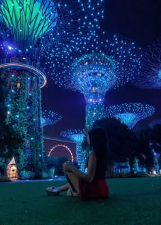 a woman sitting on the ground in front of trees with lights all over them at night