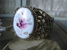 A beautifully ornate gold washed floral filigree painted glass rose cameo hinged bangle bracelet. The cameo measures 1 5/8'' x almost 1 1/4''. The bracelet measures 1 7/8'' at the widest. Also measures 2 1/2'' x 2 1/8'' across, and 7 5/8'' along the inside. In very good condition with subtle subduing of the gold. revealing the cool shiny silver underneath. Wedding Filigree Adjustable Bracelets, Adjustable Filigree Bracelets For Wedding, Antique Adjustable Wedding Bangle, Adjustable Antique Wedding Bangle, Adjustable Oval Bangle For Wedding, Antique Adjustable Cuff Bracelet For Wedding, Antique Round Cuff Bracelet For Wedding, Victorian Adjustable Bangle - Gift, Victorian Adjustable Bangle As A Gift