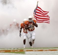 two football players running on the field with an american flag