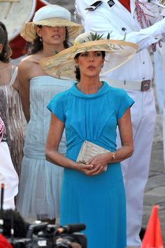 a woman in a blue dress and hat standing next to other women wearing white hats