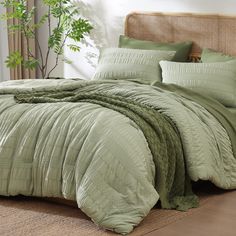 a bed with green comforters and pillows in a room next to a potted plant