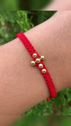 a person wearing a red bracelet with gold bells on it's wrist and green grass in the background