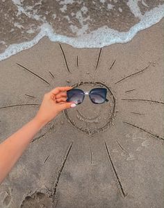 a person is holding sunglasses in the sand at the beach and drawing a heart on the sand