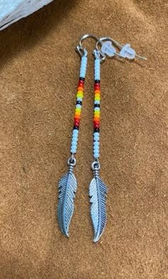 two pairs of earrings with colorful beads and feathers hanging from hooks on a brown surface