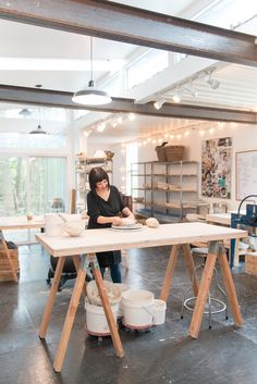 a woman sitting at a table working on pottery in a studio with lots of shelves