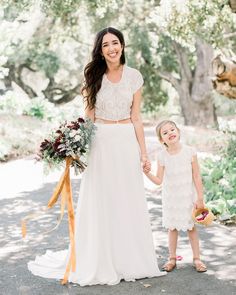 a mother and daughter holding hands while walking down the road in front of some trees