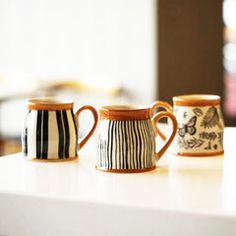 three coffee mugs sitting on top of a white counter next to each other in front of a window