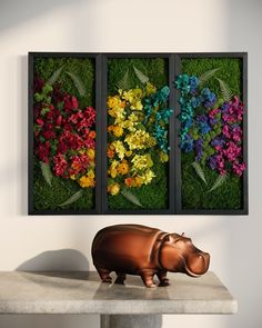 a hippo statue sitting on top of a table in front of three framed pictures