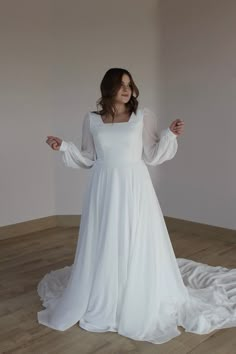 a woman in a white wedding dress standing on a wooden floor with her arms outstretched