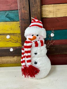 a snowman with a red and white striped scarf is standing next to a wooden wall