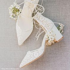 a pair of white shoes sitting on top of a gray floor next to a bouquet of flowers