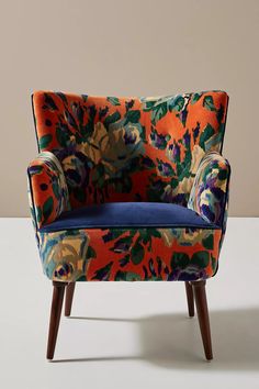 an upholstered chair with colorful fabric and wood legs on a plain surface,