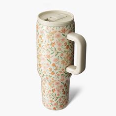 a white coffee cup with floral print on the side and handle is shown in front of a