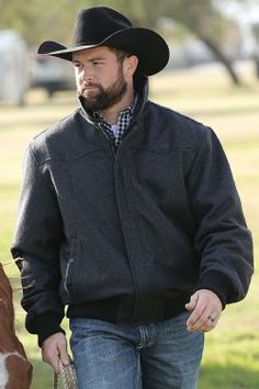 a man in a black jacket and hat walking with a brown and white horse wearing a cowboy hat