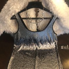 a silver and black tank top with white fur on the shoulders, in front of a hanger