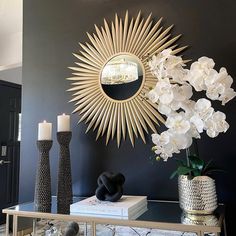 a vase with flowers and candles on a table in front of a sunburst mirror