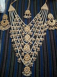 an elaborate necklace is displayed on a blue striped cloth with gold beads and pearls hanging from it