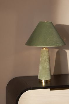 a green lamp sitting on top of a wooden table next to a white cabinet and wall