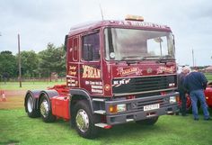 a red truck parked on top of a lush green field next to other trucks and people