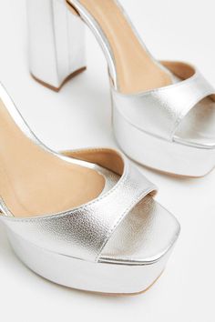 a pair of silver high heeled shoes sitting on top of a white surface