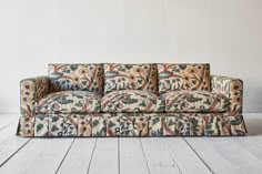 a couch sitting on top of a wooden floor next to a white wall with flowers