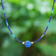 Thailand's Somluck Komolmith demonstrates her eye for fine detail and manual dexterity in this hand-beaded pendant necklace. A polished sphere of lapis lazuli commands your attention complemented by a beaded pattern featuring smaller lapis beads howlite beads and brass beads. On either side of the pendant golden hematite beads provide a visual anchor. The necklace features a spring ring clasp and extender chain of sterling silver. Lapis Lazuli Crystal Necklace With Gemstone Beads, Lapis Lazuli Gemstone Beads Crystal Necklace, Bohemian Lapis Lazuli Beaded Necklaces As Gift, Bohemian Lapis Lazuli Beaded Necklaces For Gift, Bohemian Lapis Lazuli Beaded Necklace For Gift, Sapphire Colored Lapis Lazuli Round Bead Jewelry, Sapphire-colored Lapis Lazuli Round Beaded Jewelry, Bohemian Sapphire Round Bead Jewelry, Bohemian Sapphire Beaded Jewelry