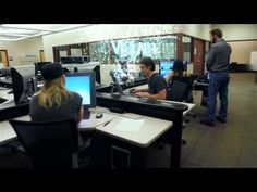 two people sitting at desks in an office setting with computers and monitors on them