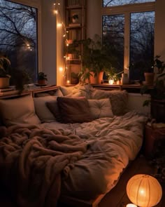 an unmade bed in front of two windows with candles on the floor next to it