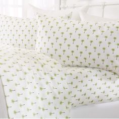 a bed with white sheets and green palm trees printed on the pillow cases, along with two pillows