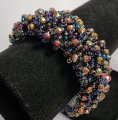 a close up of a beaded bracelet on a black display stand with white background