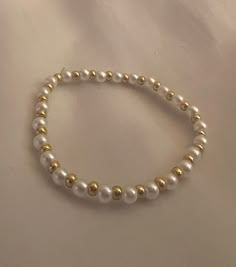 a white beaded bracelet with gold beads on a white cloth covered tablecloth,