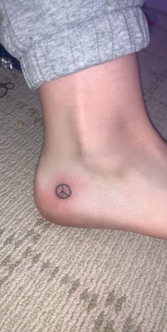 a person with a small peace sign tattoo on their foot is sitting on the floor